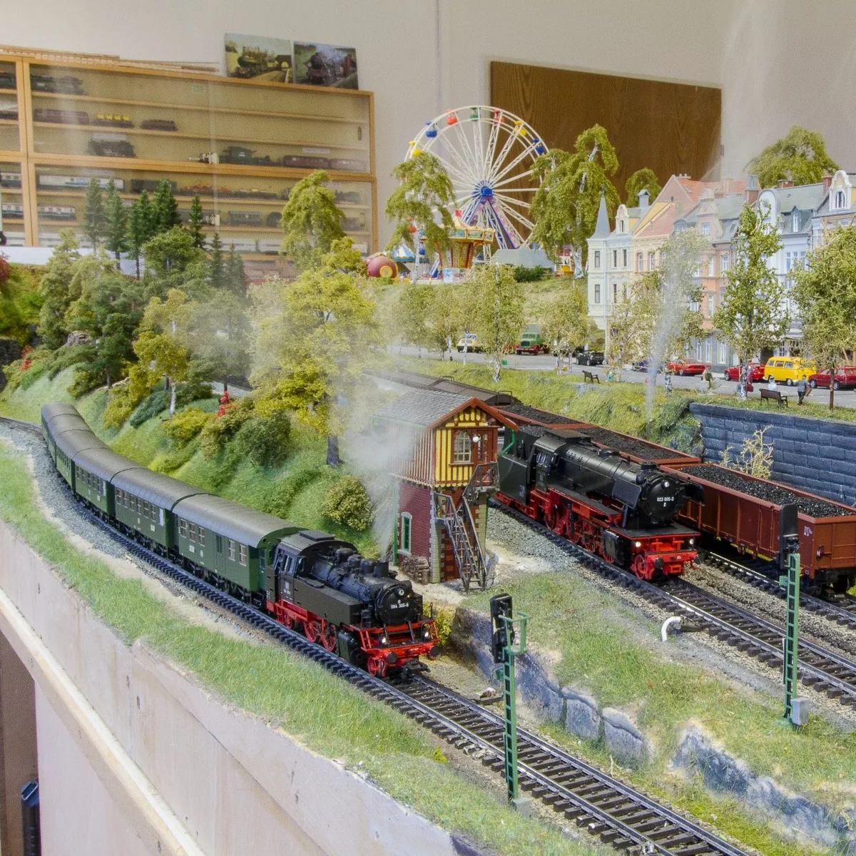 Zwei Dampfloks auf einer detailreichen H0-Modellbahnanlage mit Stadtkulisse und Riesenrad im Hintergrund