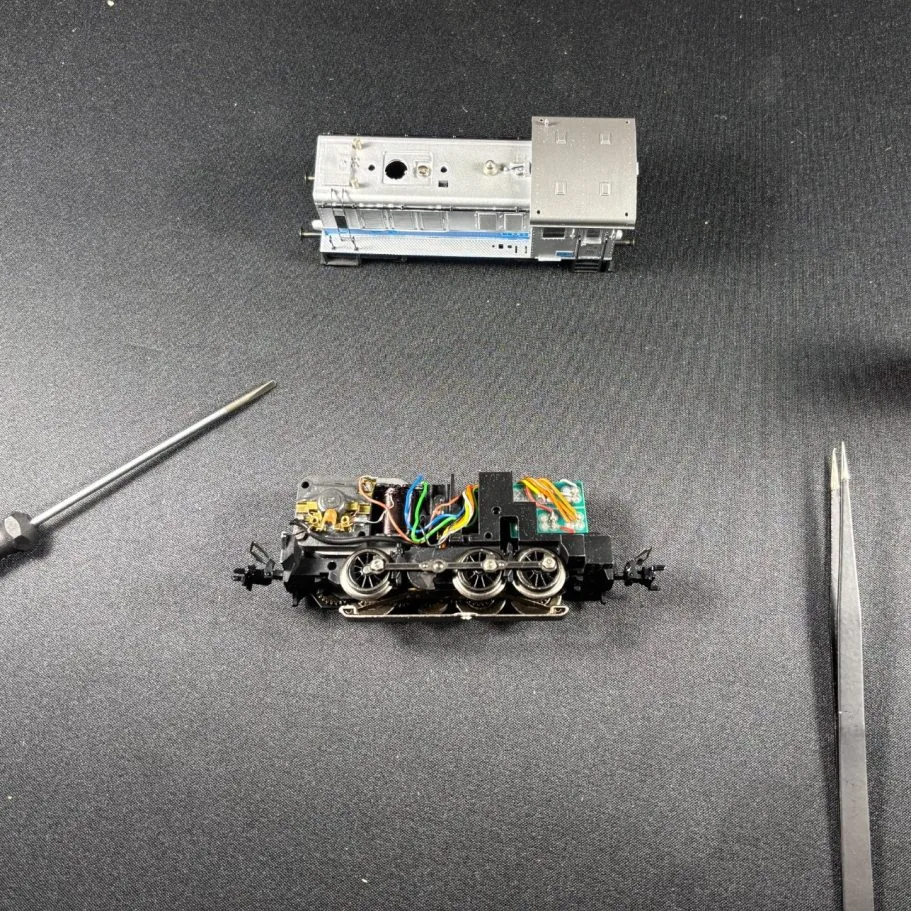 Zerlegte Modelleisenbahn-Lok mit Schraubendrehern auf schwarzem Untergrund.