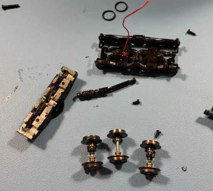Zerlegtes Fahrwerk einer Märklin NoHAB 204 vor der Reinigung: links der Getriebeblock mit dunklem, verharztem Altfett, daneben Schneckenwelle, Drehgestellrahmen und Radsätze.