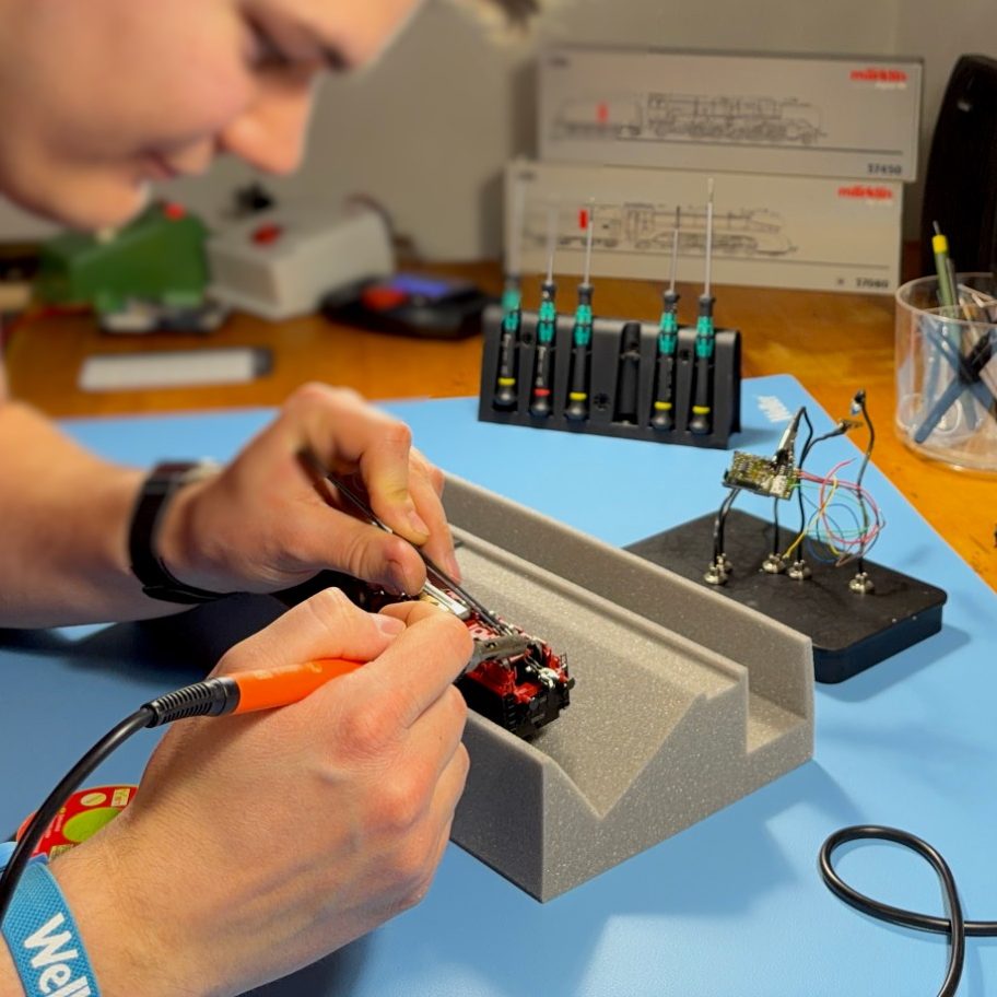 Junger Mann in einer Werkstatt für Modelleisenbahnen repariert eine Modellbahn.