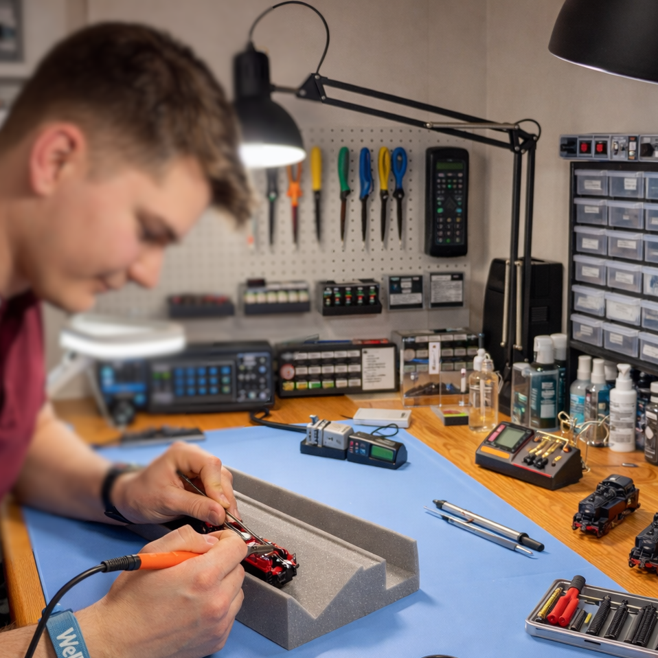 Junger Mann in einer Werkstatt für Modelleisenbahnen repariert eine Modellbahn.