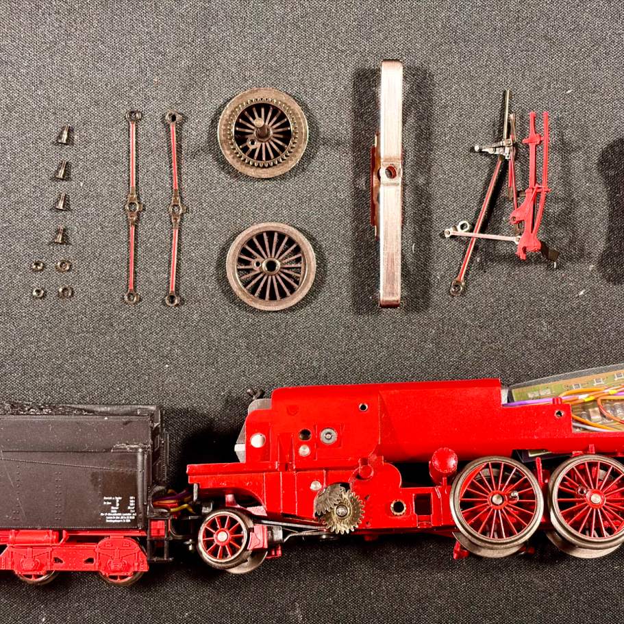Modellbahnkomponenten mit einer zerlegten Lokomotive und mehreren Einzelteilen auf einem Tisch.