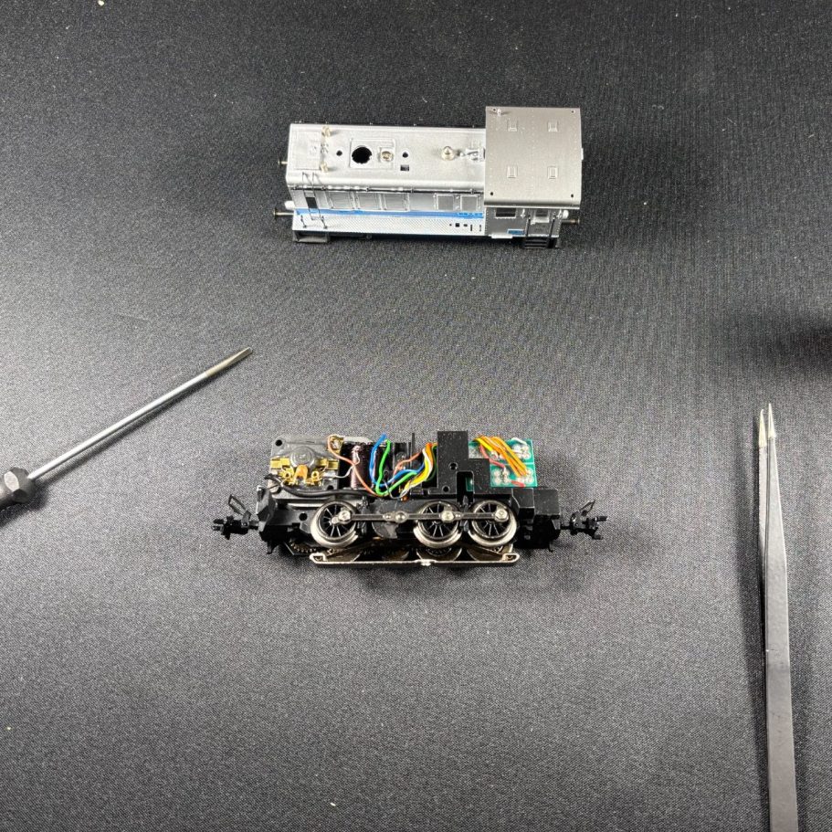 Zerlegte Modelleisenbahn-Lok mit Schraubendrehern auf schwarzem Untergrund.